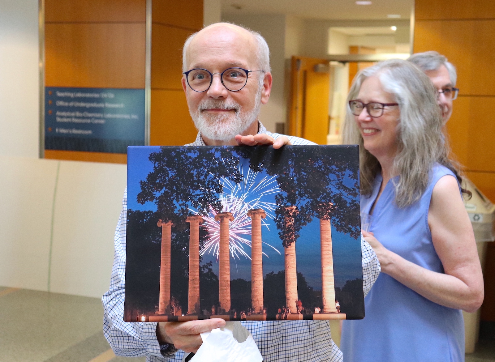 Thomas Phllips holds up a painting of Columns with fireworks over them.