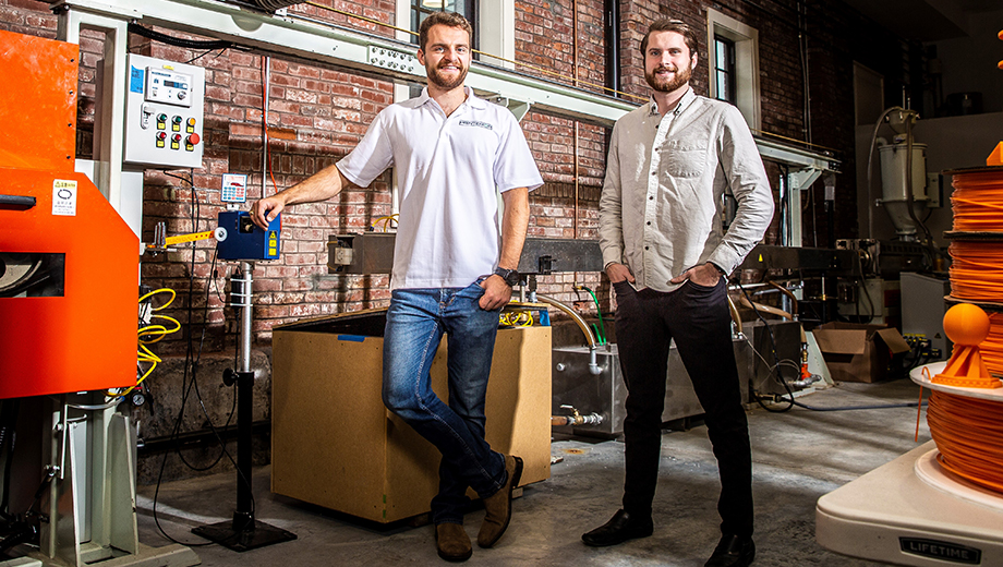 Hayden Seidel (left) and Trent Esser (right) stand in front of the production line used to launch their first 3D-printed filament products made from recycled materials. In 2020, they won $5,000 from EQ.