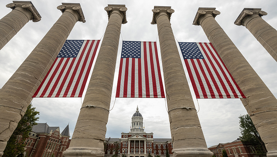 Three U.S. flags adorn the Columns with Jesse Hall in the background.