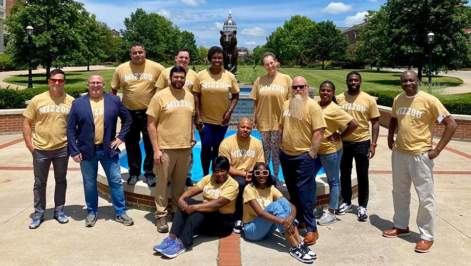 A group of EBV graduates pose in Mizzou shirts by a fountain.