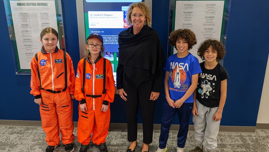 Keynote speaker Sandra Magnus, former astronaut, poses with four youth dressed in NASA gear.