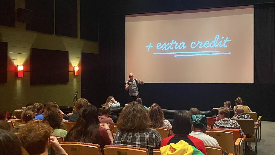 The Extra Credit film series, presented by the Division of Research, Innovation & Impact’s The Connector and hosted by Ragtag Cinema, explores popular films through an academic lens. An audience awaits a showing of "School of Rock" in a dim theater.