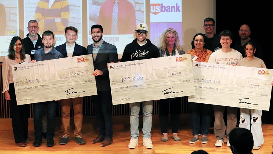 EQ winners holding oversized checks pose with judges.