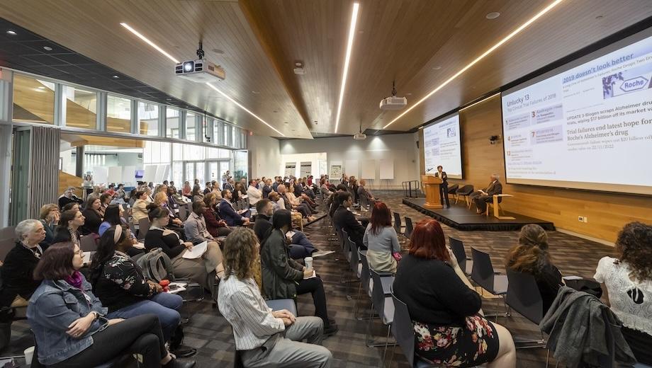 MU School of Medicine Professor Smita Saxena addresses the PATHWAYS symposium. People in rows of chairs listen to Smita, who is on a stage with large TV screens behind her.