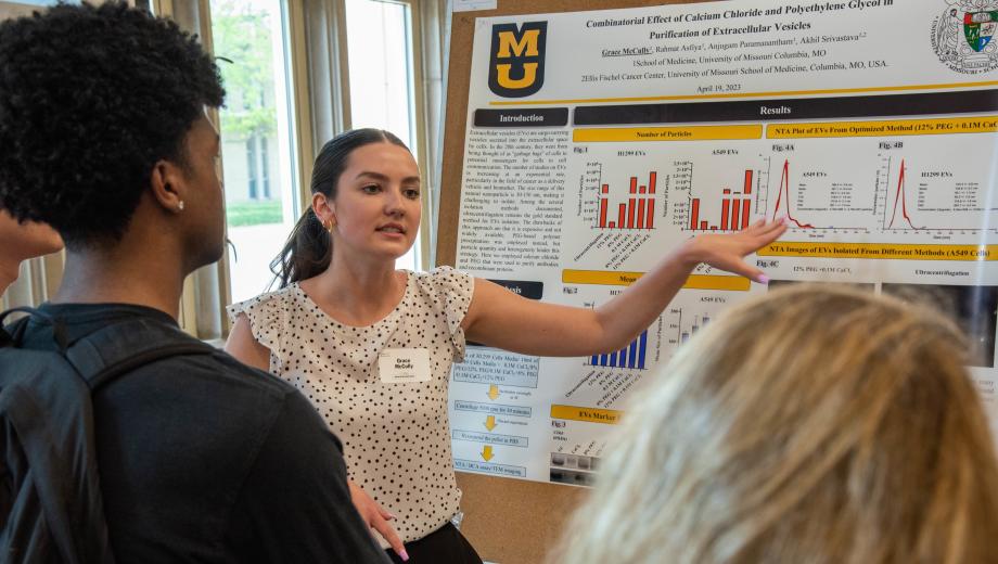 A University of Missouri student points toward her research poster while discussing her research in the School of Medicine.