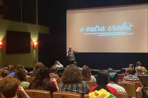 The Extra Credit film series, presented by the Division of Research, Innovation & Impact’s The Connector and hosted by Ragtag Cinema, explores popular films through an academic lens. An audience awaits a showing of "School of Rock" in a dim theater.